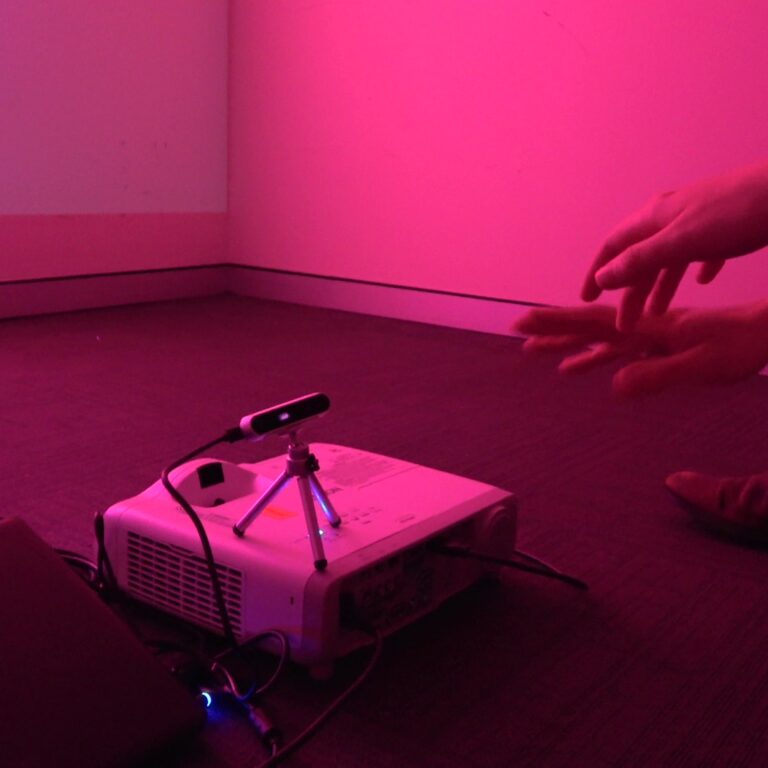 Two hands stretch towards a depth sensor positioned above a projector.